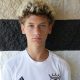 Young man in white soccer uniform posing for a portrait.