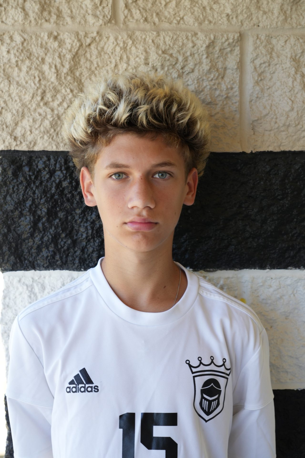 Young man in white soccer uniform posing for a portrait.