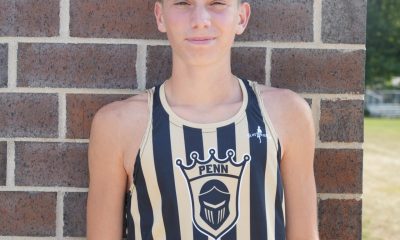Young man in tank top posing against brick wall.