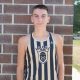 Young man in tank top posing against brick wall.