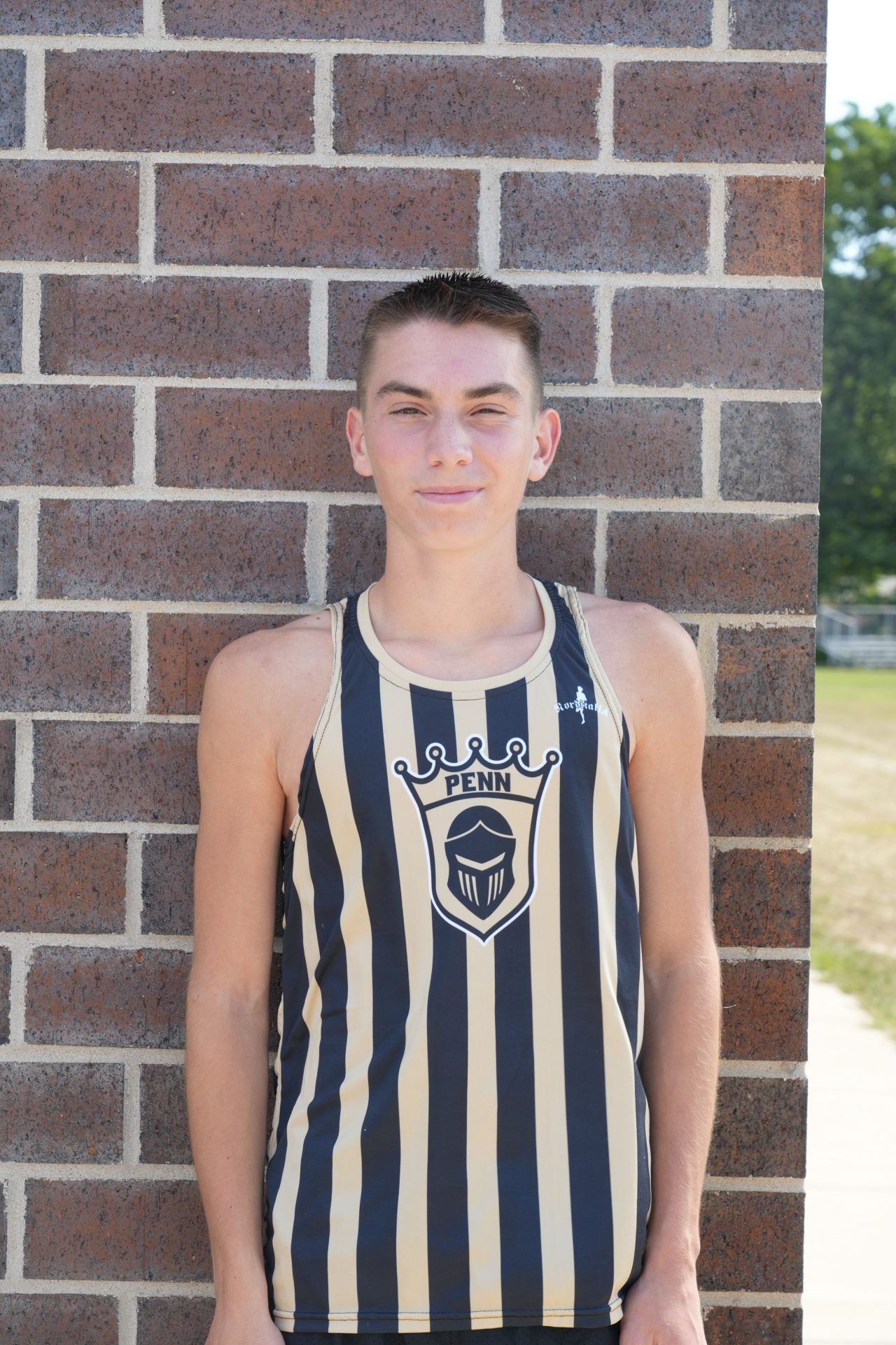 Young man in tank top posing against brick wall.