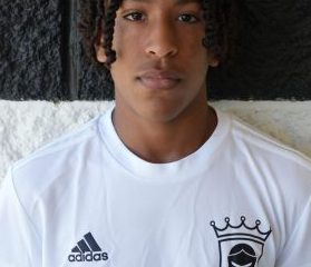 This is a portrait of a person wearing a soccer uniform. The individual has dreadlocks and is looking directly at the camera.