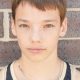 Young man in black and white striped tank top standing against brick wall.