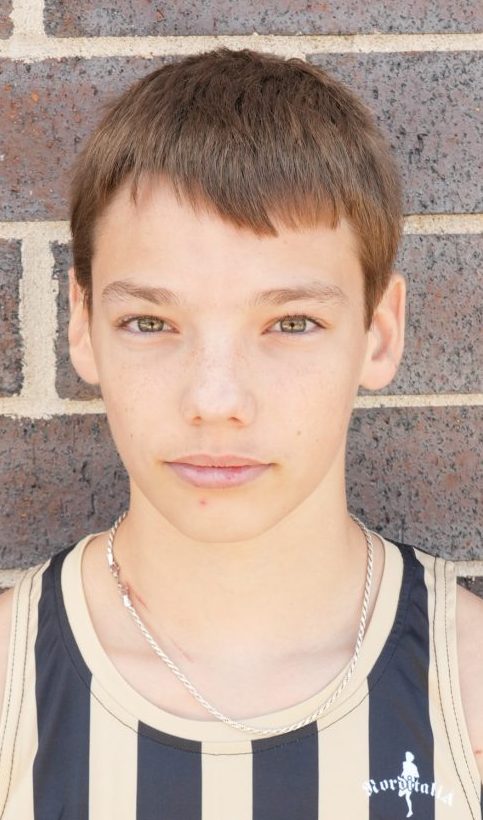Young man in black and white striped tank top standing against brick wall.