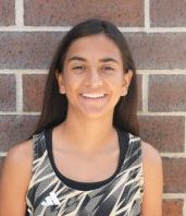Girl posing in front of brick wall, smiling at camera.