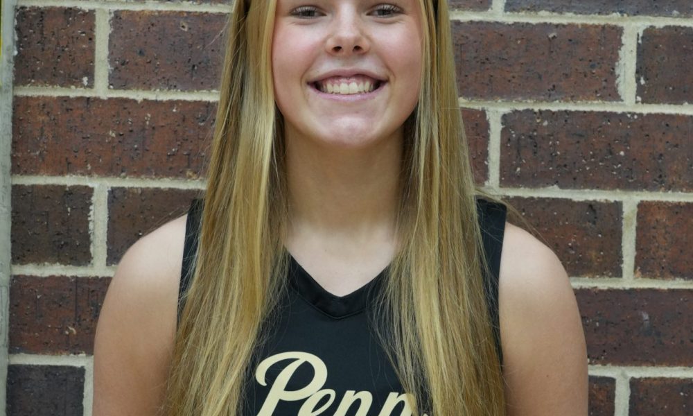 Girl in black jersey posing for picture against brick wall.