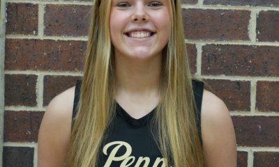 Girl in black jersey posing for picture against brick wall.