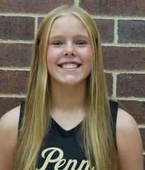 Girl in black jersey posing for picture against brick wall.