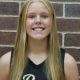Girl in black jersey posing for picture against brick wall.