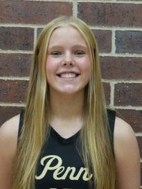 Girl in black jersey posing for picture against brick wall.
