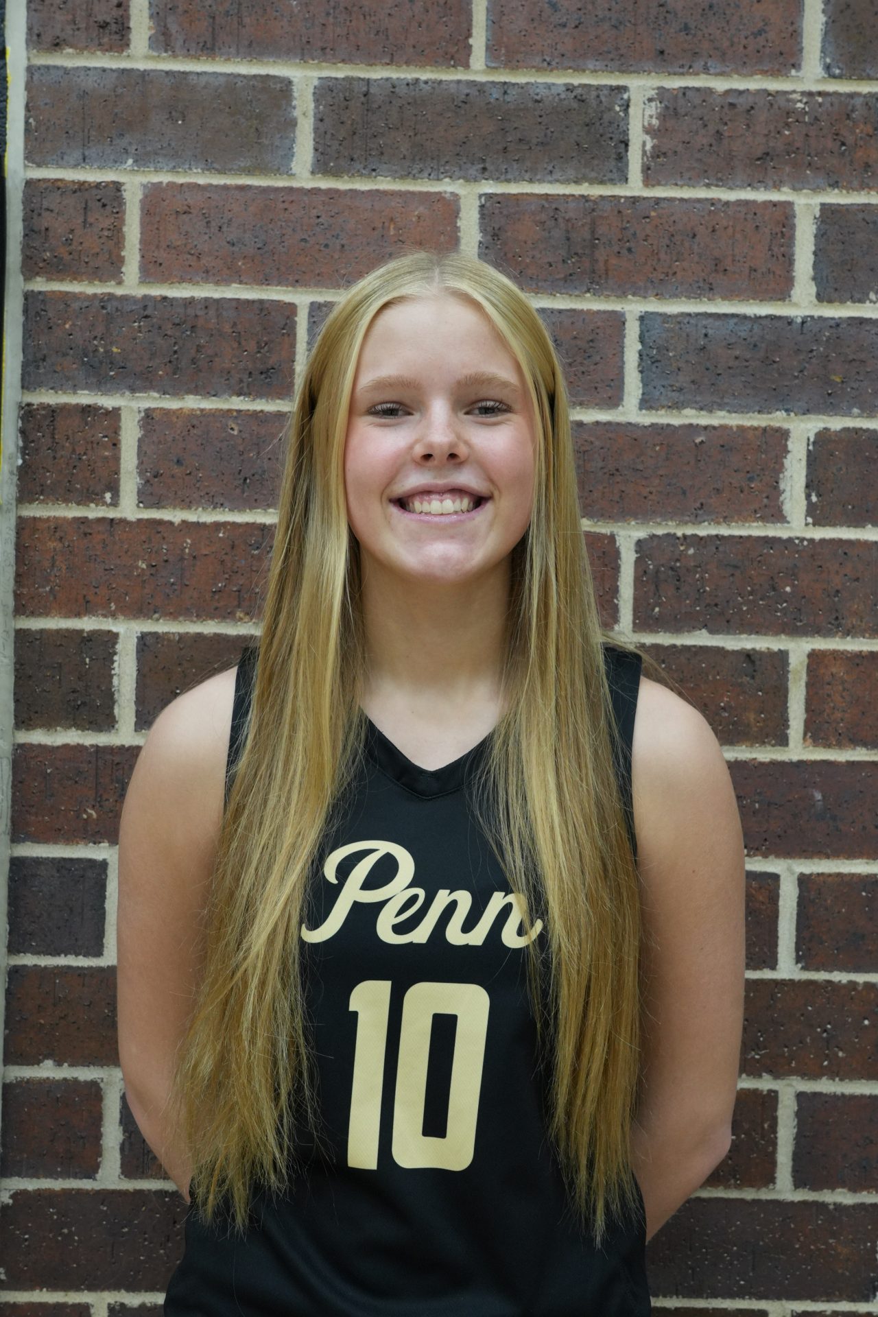 Girl in black jersey posing for picture against brick wall.