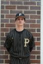 Baseball player in uniform standing against brick wall.