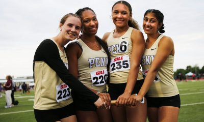 Four female athletes posing together on a football field.