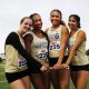 Four female athletes posing together on a football field.