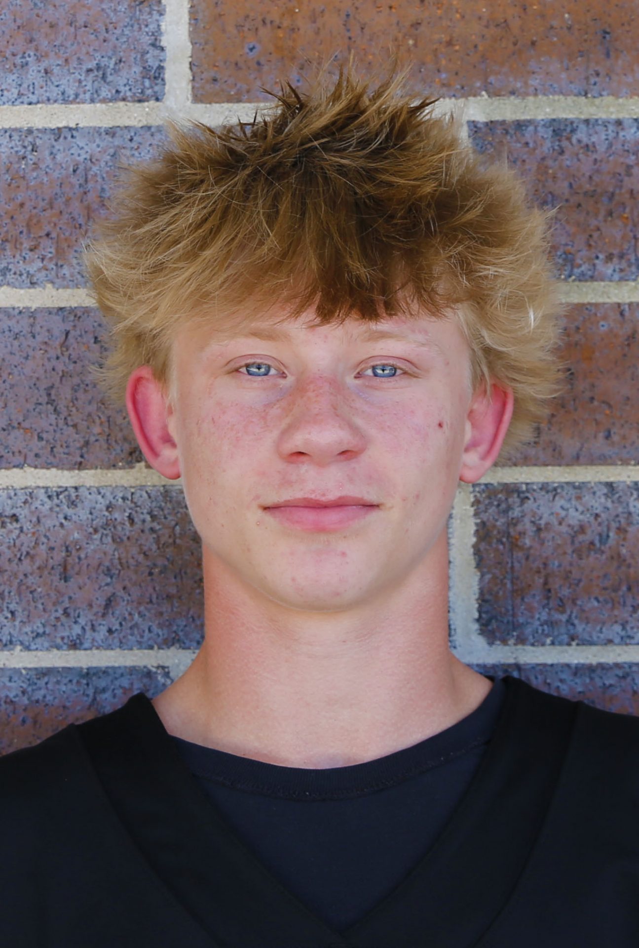 Young man with spiky hair posing for a portrait against a brick wall.