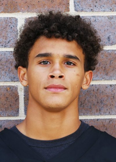 Young man in black and white portrait against brick wall.