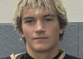 This is a portrait of a young man with blonde hair wearing a hockey uniform. He has a serious expression on his face and is