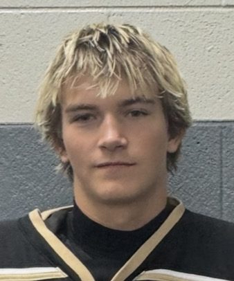 This is a portrait of a young man with blonde hair wearing a hockey uniform. He has a serious expression on his face and is