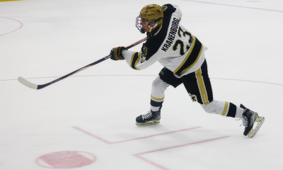 Hockey player in mid-action, holding a stick and wearing a helmet, skating on an ice rink.