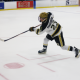 Hockey player in mid-action, holding a stick and wearing a helmet, skating on an ice rink.