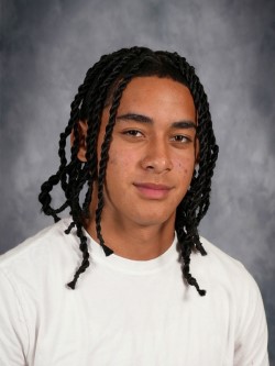Young male with dreadlocks wearing a white t-shirt and braided hair, posing for school portrait.