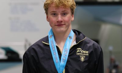 Male swimmer in a pool competition, posing for a photo, wearing a medal around his neck and a jacket.