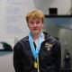 Male swimmer in a pool competition, posing for a photo, wearing a medal around his neck and a jacket.