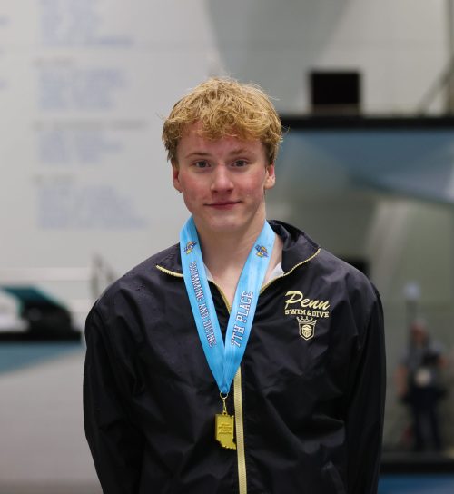 Male swimmer in a pool competition, posing for a photo, wearing a medal around his neck and a jacket.