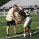 Coach O'Connell on the football field during practice showing a player how to hold a football.