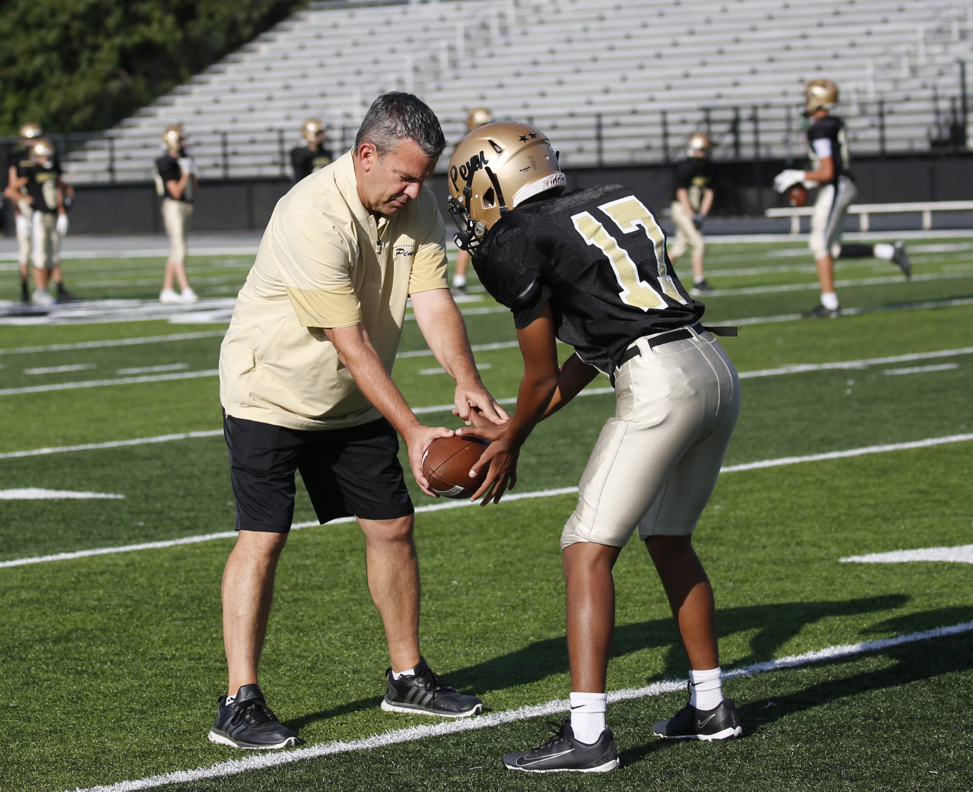 Coach O'Connell on the football field during practice showing a player how to hold a football.