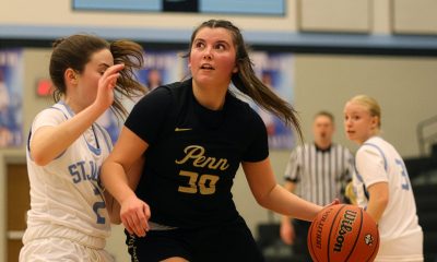 Two girls playing basketball on a court. One girl is in motion, holding a ball, while the other girl is standing and looking