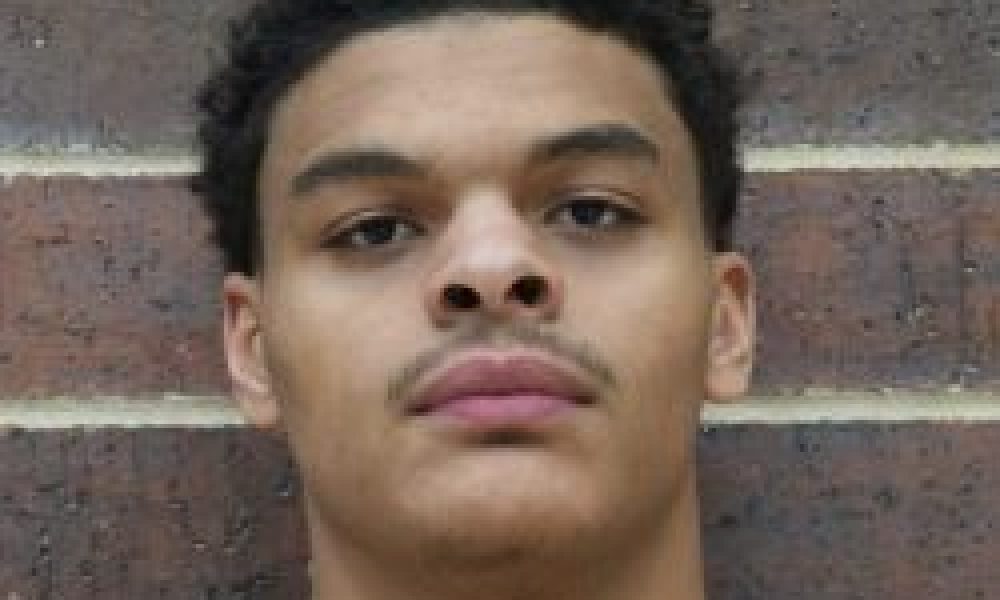 Man wearing basketball uniform posing against brick wall.