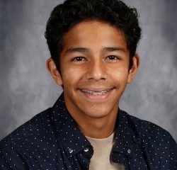 This is a portrait of a young man posing for a school picture. He has short hair and is wearing a blue shirt.