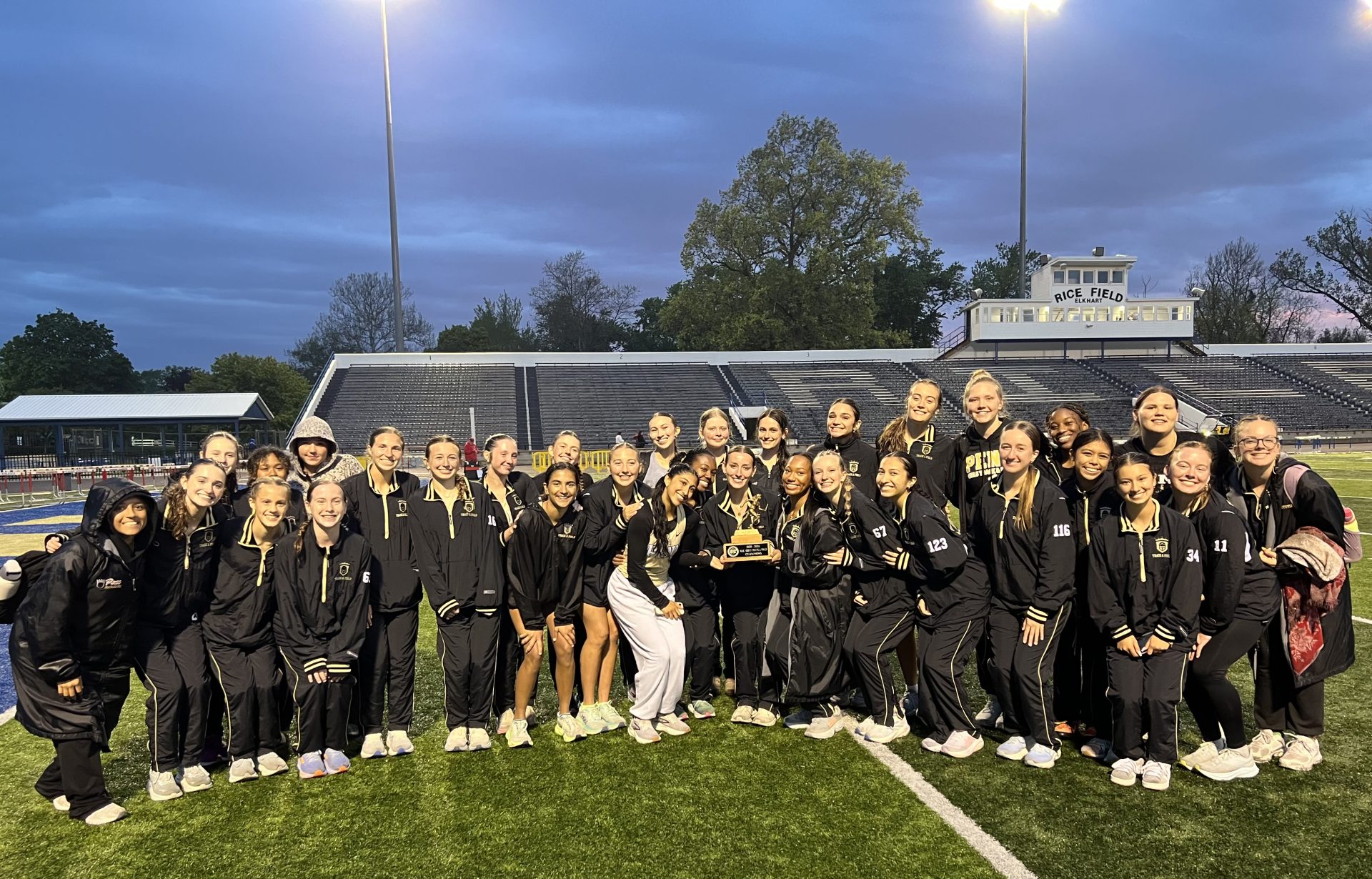 Penn Girls Track & Field team posing with a trophy on a track infield.