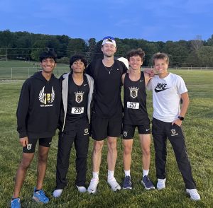 Four track runners posing together in front of a field.