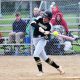Woman swinging baseball bat on field.