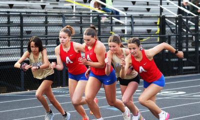 Female runners in a race, all wearing red uniforms, sprinting on a track.