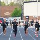 Athletes in uniforms running on a track.