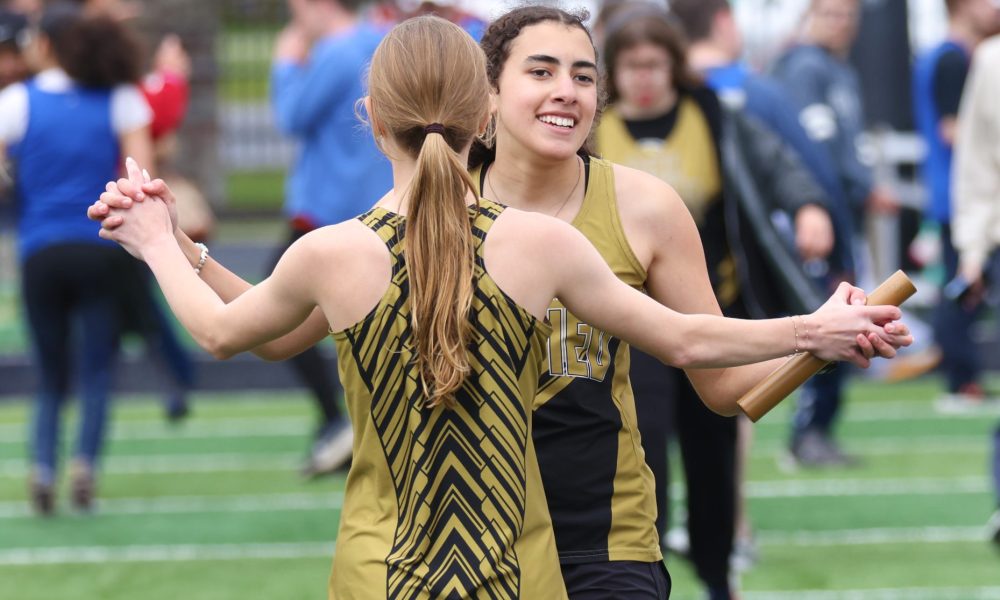 Two women in black and yellow uniforms hugging on a football field.