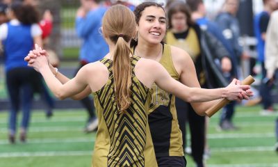 Two women in black and yellow uniforms hugging on a football field.