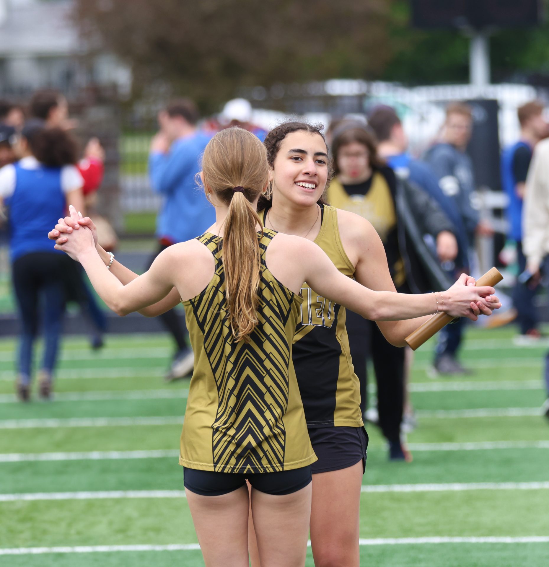 Two women in black and yellow uniforms hugging on a football field.