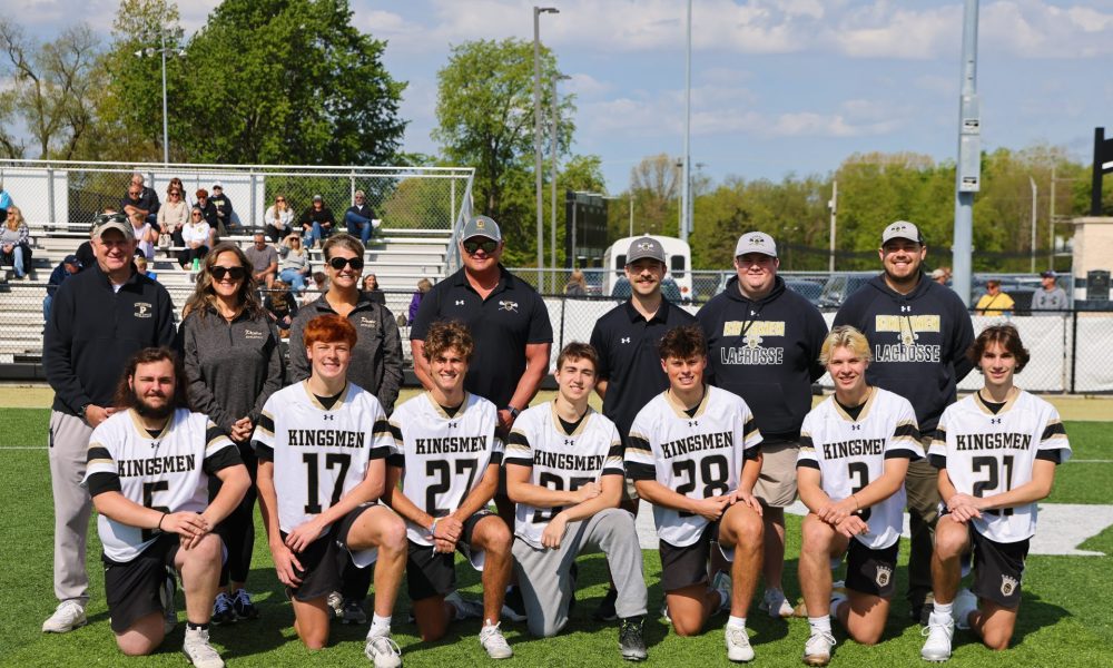 Group of young men in football uniforms posing for a team picture on a football field.
