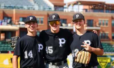Three baseball players posing together on a field.