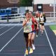 Female runner in yellow shoes leading a group of runners on a track.