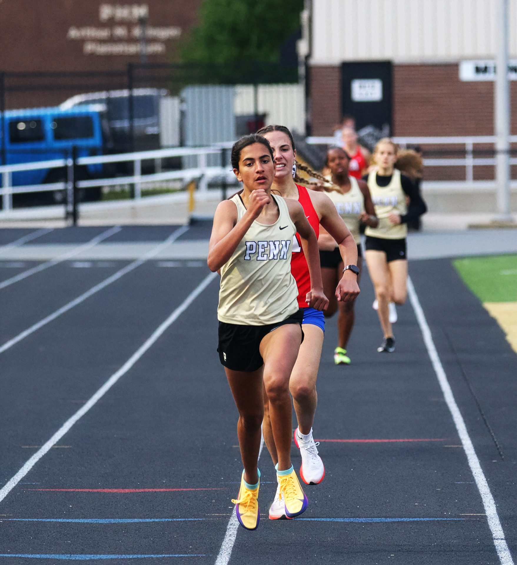 Female runner in yellow shoes leading a group of runners on a track.