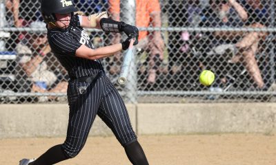 Softball player in black and white uniform swinging bat at ball during game.