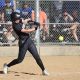 Softball player in black and white uniform swinging bat at ball during game.