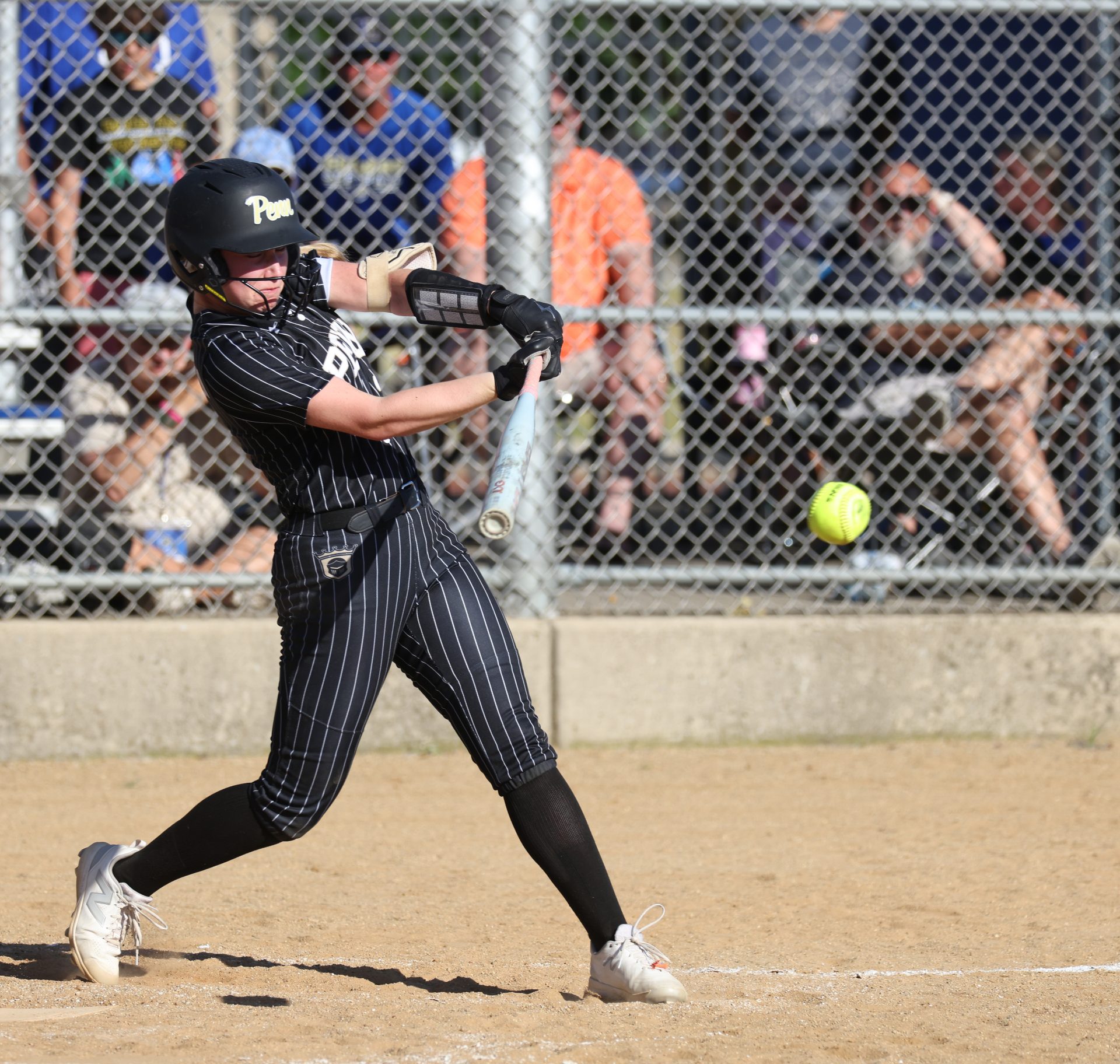 Softball player in black and white uniform swinging bat at ball during game.