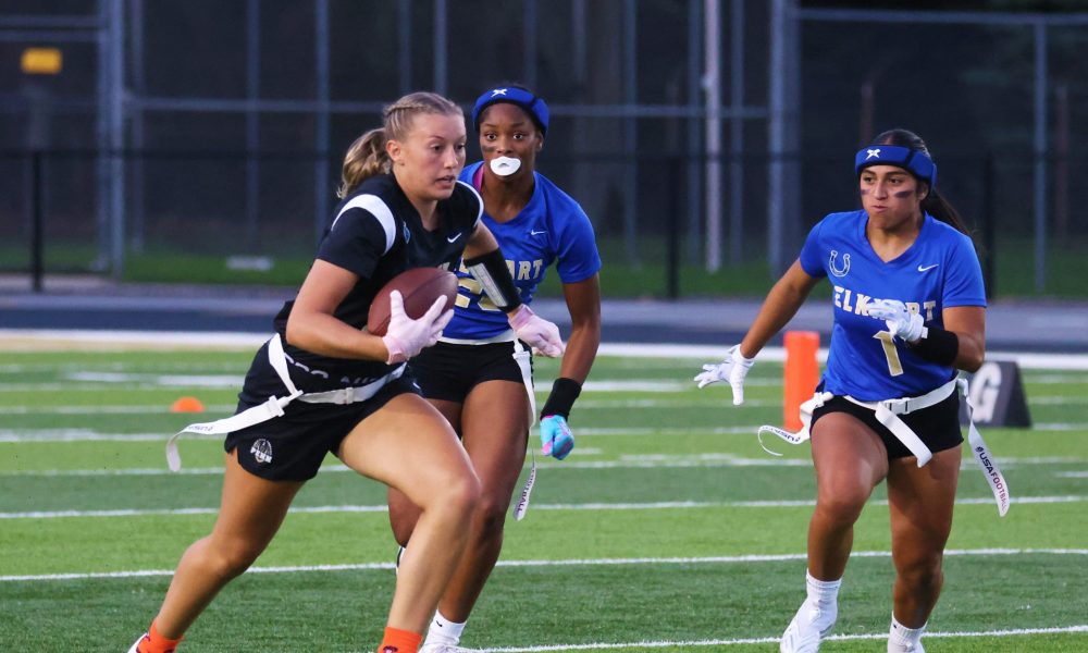 Female athlete in action, running with football in hand, during nighttime game on field, with teammates and