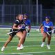 Female athlete in action, running with football in hand, during nighttime game on field, with teammates and